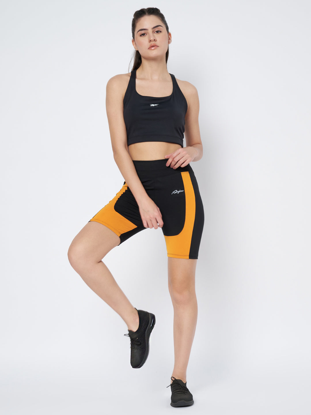 Dynamic pose of a model in Waylene's black and orange sports shorts, demonstrating flexibility and comfort of the shorts, suitable for fitness routines.