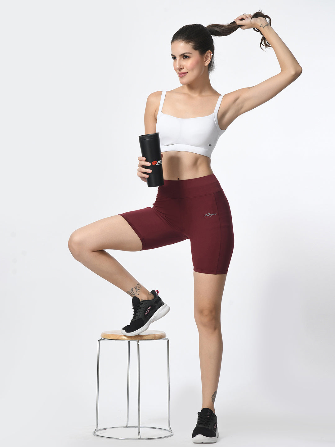 Waylene wine-colored high-performance shorts with pocket, women's activewear, model posing with a bottle.